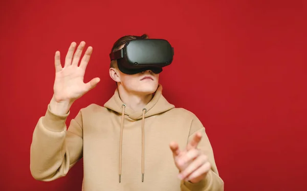 Jeune homme debout sur fond rouge avec casque VR sur la tête et toucher de côté sur l'espace de copie. Il utilise un casque de réalité virtuelle. Isolé. Concept VR — Photo