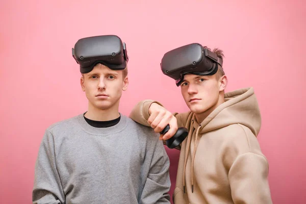 Deux jeunes gars en réalité virtuelle casques isolés sur fond rose regardant dans la caméra avec un visage sérieux. Les joueurs adolescents dans les casques VR isolés sur fond rose . — Photo