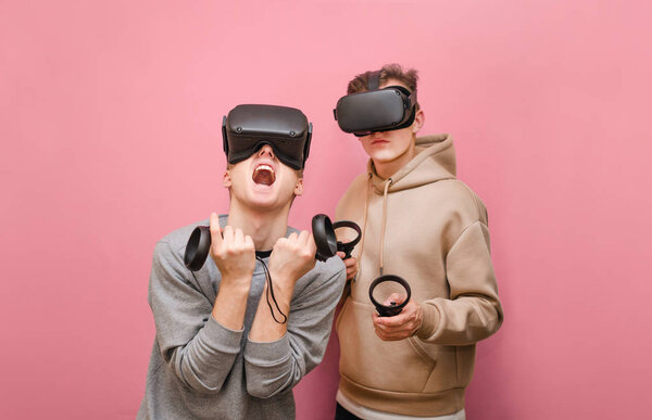 Портрет эмоциональных 2 молодых людей в шлемах VR на розовом фоне, играющих в игры виртуальной реальности на коньках в руках. Пара выразительных друзей, играющих в виртуальные игры на консоли
.