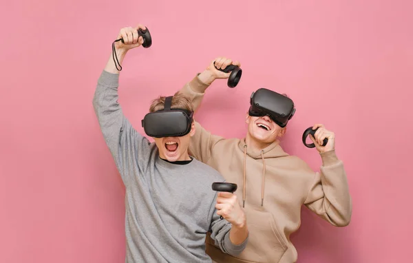 Deux amis joyeux dans les casques VR profiter de gagner le jeu. 2 gars équipe jouant VR jeux sur fond rose. Isolé. Loisirs entre amis en réalité virtuelle. Jeux VR — Photo