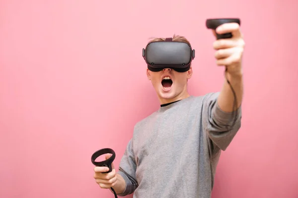 Jeune homme émotionnel portant un casque VR sur la tête et vêtements décontractés jouer à des jeux de réalité virtuelle avec des contrôleurs dans ses mains, regardant dans la caméra avec la bouche ouverte. Génération de jeux VR — Photo