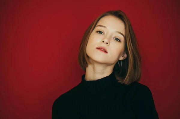 Primer plano retrato de chica en ropa casual, vistiendo suéter negro, aislado sobre fondo rojo, se ve enfocado en la cámara. Hermosa modelo de niña posando en la cámara, foto de primer plano en la pared roja — Foto de Stock