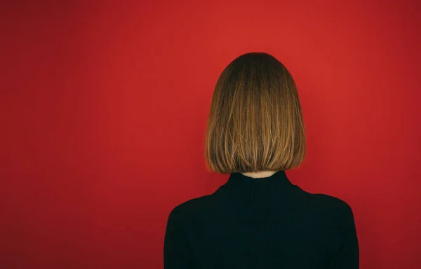 Meisje met bob kapsel staat met haar rug tegen een rode achtergrond. Vrouw met kort haar geïsoleerd op rood, bob kapsel. Kopieerruimte — Stockfoto
