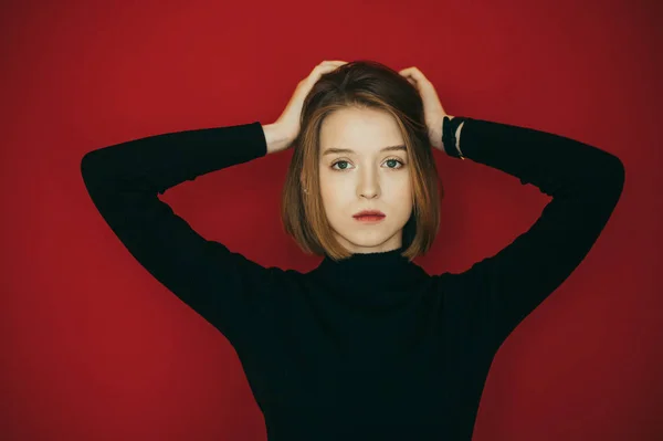 Primer plano retrato de modelo en ropa casual, vistiendo suéter negro, aislado sobre fondo rojo, se ve enfocado en la cámara. Hermosa modelo de niña posando en la cámara, foto de primer plano en la pared roja — Foto de Stock