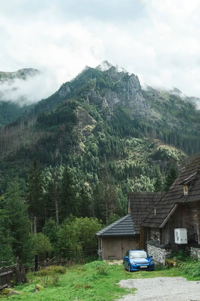 Dağlarda ahşap bir ev ve mavi bir araba güzel kayalık bir manzaranın arka planında. Dağlardaki kır evinin dikey fotoğrafı. Ulusal rezerv içindeki kulübe. — Stok fotoğraf