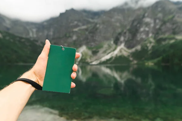 A mão do homem segura uma túrgida verde em branco contra o fundo do Lago Morskie Oko, ou Olho do Mar nas Montanhas Tatra, no sul da Polônia. Espaço para cópia. Espaço vazio. — Fotografia de Stock