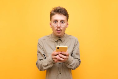 Gözlüklü ve bıyıklı şaşırmış bir adam sarı arka planda elinde akıllı telefonla kameraya bakıyor. Sarı arka planda izole edilmiş akıllı telefonu kullanan şaşırmış bir Batman portresi.