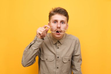 Sarı arka planda şaşırmış bir ineğin portresi, gözlüğünü çıkarıyor ve şok olmuş bir şekilde kameraya bakıyor. Zayıf görüşlü bir adam kameraya şok edici bir şekilde bakar. Sarı arkaplanda izole edilmiş.