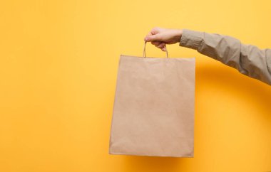 İnsan eli sarı bir arka planda elinde bir kese kağıdı tutar. Kraft paketinde gömlekli bir adam var. İzole edilmiş. Ekolojik kağıt alışveriş torbası bir adamın elinde. Boşluğu kopyala