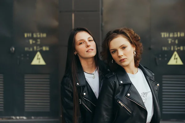 Retrato de rua de dois modelos em um fundo preto, usando jaquetas de couro e olhando atentamente para a câmera, de perto. Casal de meninas posando para a câmera no fundo urbano escuro . — Fotografia de Stock