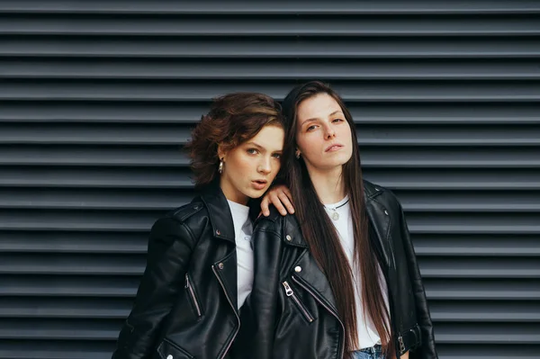 Retrato elegante de dois modelos com sardas em roupas casuais em um fundo de rua escuro, usando jaquetas de couro, olhando para a câmera com um rosto sério.Menina posando para a câmera na parede escura — Fotografia de Stock