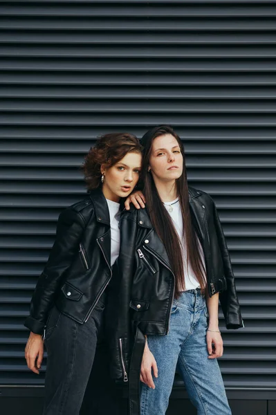 Модний портрет двох моделей з веснянками в повсякденному одязі на темному вуличному тлі, одягнений в шкіряні куртки, дивиться в камеру з серйозним обличчям. Дівчина позує на камеру на темній стіні — стокове фото