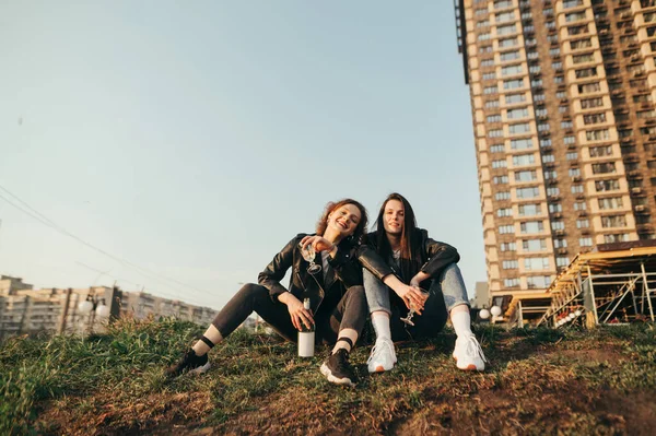 Portrait of happy young girls in leather jackets sitting on gras — Stock Photo, Image