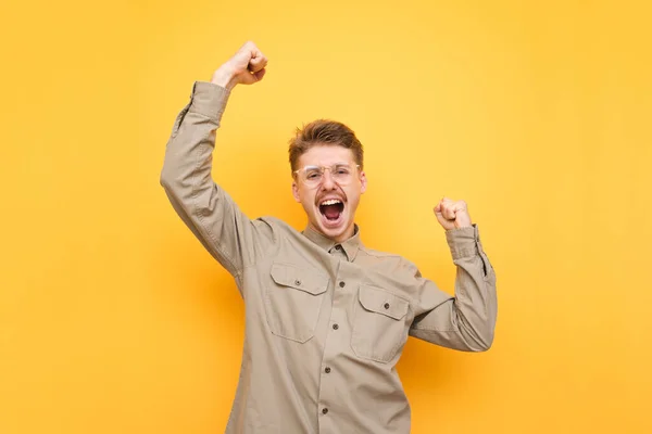 Портрет радостного молодого человека в рубашке на желтом фоне, радующегося победе с поднятыми руками и криками. Ботаник в очках и усах победил, с радостью отреагировав на победу. Isolated . — стоковое фото