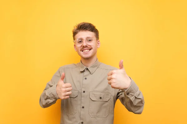 Портрет счастливого ботана в очках и бежевой рубашке стоит на жёлтом фоне, показывает большие пальцы вверх и смотрит в камеру с улыбкой на лице. Радостный парень с усами показывает как жест. Копирование пространства — стоковое фото