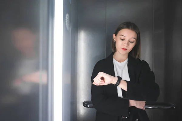 Vrouwelijke beambte is moe van het wachten in de lift. Jonge werknemer is kijken naar haar horloge verveeld wachten in de lift. — Stockfoto