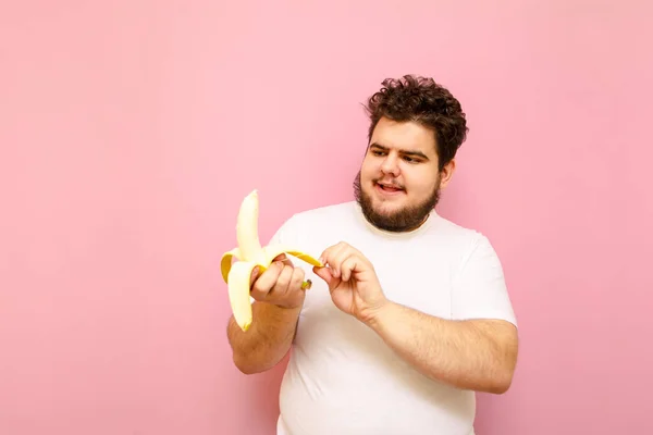 Портрет Смешного Толстяка Белой Футболке Розовом Фоне Показывает Банан Выглядит — стоковое фото