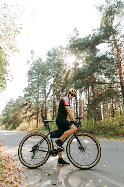 Man with bicycle standing on road on forest background at sunset, looking down. Man on a bicycle walk in the forest, stands resting. Professional cyclist trains on forest road.