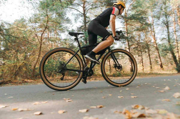 Photo of a professional cyclist moving fast on a forest road. A man is actively training on a bicycle in the park in the autumn day. Cycling is a hobby.