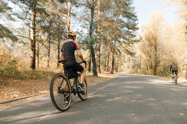 骑自行车的人背靠在森林的路上 背景是秋天的风景 一个头戴头盔 身穿自行车衣服的男人骑自行车 骑完车后休息 周末自行车业余爱好 — 图库照片