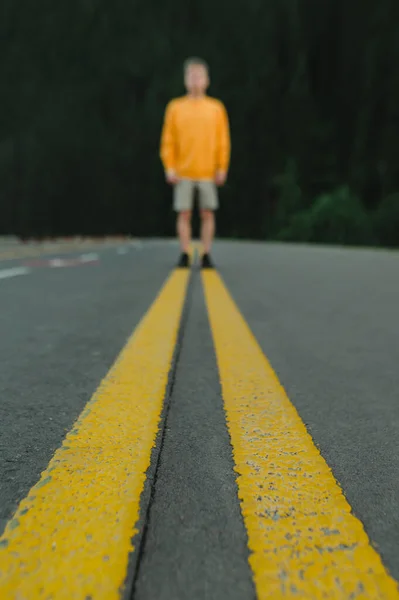 Abstract blurred photo. Background. Vertical. Asphalt forest road with yellow markings on blurred man\'s background in orange sweater. Copy space