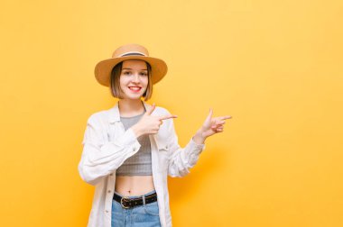 Açık yaz elbisesi ve şapkası içinde gülümseyen turist kız fotokopi odasında el ele tutuşuyor ve mutlu bir yüzle kameraya bakıyor. Sarı arka plandaki neşeli bayan boş alana parmak gösteriyor..