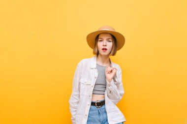 Sarı arka planda dans eden açık renk elbiseli ve şapkalı güzel bir kız. Dans eden ve kameraya bakan çekici turist kız, turuncu arka planda izole edilmiş.