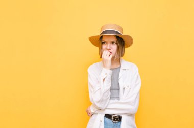 Hafif giysili ve şapkalı dalgın üzgün kız sarı arka planda izole edilmiş, fotokopi odasına bakıyor ve düşünüyor. Sarı arka planda güzel bir bayan.