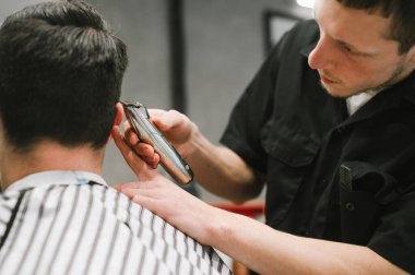 Profesyonel berber, elinde altın makasıyla ve yakın plan fotoğrafıyla müşteri için şık bir saç stili yaratıyor. Altın kesicili bir berberin elleri esmer bir adamın saçını keser.