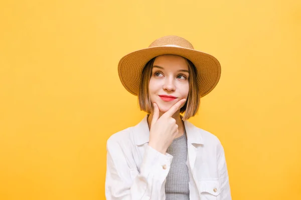 Closeup pretty pensive woman in light clothing on yellow background, isolated on yellow background, looking aside with pensive positive face and hand on beard.Thoughtful girl on a yellow background