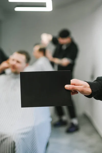 Mężczyzna Trzyma Pustą Czarną Kartę Dla Copyspace Tle Męskiego Fryzjera — Zdjęcie stockowe