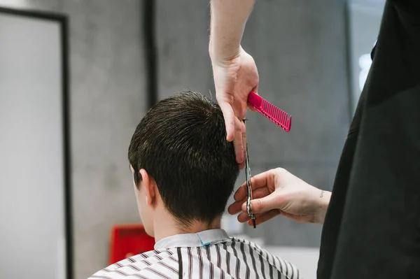 Professional barber cuts the client's hair with scissors in a barber shop, close photo. Creating a fashionable men's haircut with the help of scissors and a comb in the hands of a master. Copy space