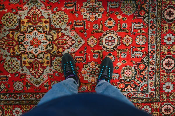 Man stands on the carpet and takes a photo of his feet. Fashionable sneakers on her feet and wears jeans. Background. Photo of legs with sneakers and jeans, top view, standing on the carpet.