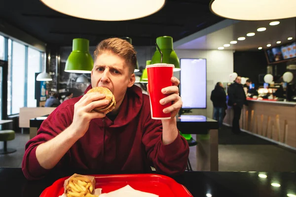 젊은이는 패스트푸드 식당에 음식을 맛있는 햄버거를 껴안고 카메라를 바라본다 패스트 — 스톡 사진