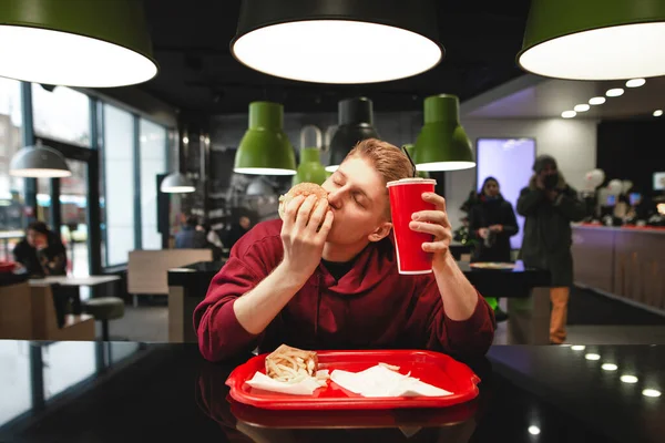 Joven Hambriento Sienta Mesa Restaurante Comida Rápida Muerde Una Hamburguesa — Foto de Stock