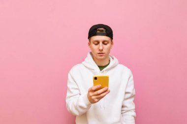 Normal giyinmiş konsantre bir adam pembe bir arka planda elinde akıllı bir telefonla ciddi bir yüzle ekrana bakar. Odaklanmış genç adam akıllı telefonlarda internet kullanıyor. İzole edilmiş