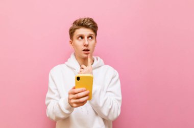 Beyaz kapüşonlu düşünceli bir adamın portresi pembe arka planda elinde akıllı telefonuyla dikiliyor ve dalgın bir suratla başka yere bakıyor. Ergen akıllı telefon kullanır, fotokopi alanına bakar ve düşünür ki....