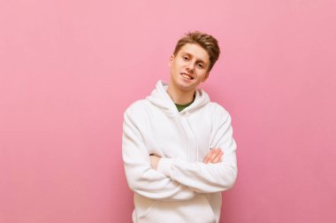 Beyaz elbiseli, gülümseyen sarışın adam pembe arka planda kameraya poz veriyor ve mutlu bir yüz ile kameraya bakıyor. Pembe arka planda izole edilmiş neşeli öğrenci. Boşluğu kopyala