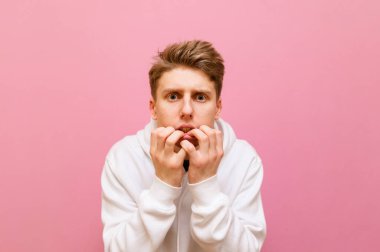 Pembe arka planda korkmuş genç bir adamın yakın plan portresi. Şok olmuş yüz ifadesiyle kameraya bakıyor. Beyaz kapüşonlu garip adam pembe arka planda izole edilmiş. Boşluğu kopyala