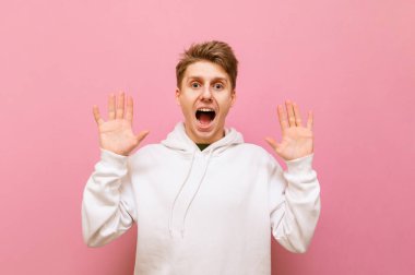 Pembe arka planda açık renk bir süveter giymiş korkmuş bir çocuğun portresi korkmuş bir yüzle kameraya bakıyor ve avuç içleri korku içinde ellerini kaldırıyor. Şok olmuş genç bir adam ağzı açık kaldı.