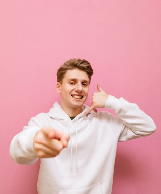 Beyaz kazaklı, gülümseyen adam pembe arka planda jest yapmamı söylüyor, mutlu yüzlü kameraya bakıyor. Neşeli adam çınlayan bir jest ve sana bir parmak gösteriyor. Boşluğu kopyala