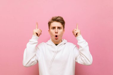 Şok olmuş, beyaz günlük elbiseli sarışın bir çocuğun portresi pembe bir arka planda duruyor, kameraya bakıyor ve boş bir yeri işaret ediyor. Şaşırmış genç adam fotokopi alanında boy gösteriyor.