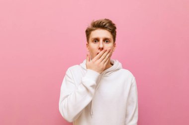 Şaşkın genç adam pembe bir arka planda duruyor ve şaşırmış bir yüzle kameraya bakıyor. Şaşırmış öğrenci pembeye izole edilmiş, ağzını şoktan kapamış, boşluğu kopyalamış.