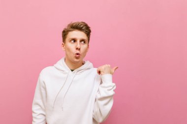 Beyaz giysili komik sarışın adam şok olmuş bir ifadeyle kafasını çeviriyor ve fotokopi alanını işaret ediyor. Pembe arka planda izole edilmiş, boş alanı işaret eden şaşırmış bir gencin portresi..