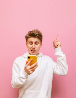 Huysuz ve komik suratlı şaşırmış bir adam akıllı telefon kullanıyor ve parmağını fotokopi alanına doğrultuyor. Akıllı telefonlu üzgün bir genç boş alanda parmağını gösteriyor. Dikey portre. Boşluğu kopyala