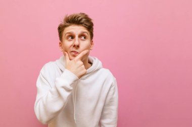 Pembe arka planda izole edilmiş komik genç adam, düşünceli yüzüyle fotokopi alanına bakıyor. Düşünceli adam pembe arka planda duruyor ve komik bir suratla boş alana bakıyor. Boşluğu kopyala