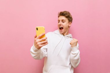 Elinde akıllı telefon olan neşeli bir adam pembe arka planda kazanmaktan duygusal olarak memnun. İzole edilmiş.
