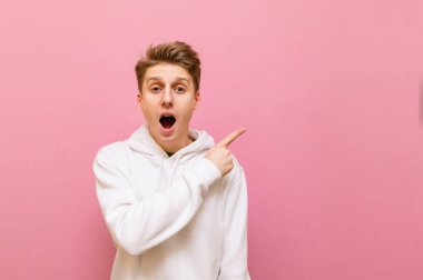 Şok olmuş bir ifadeyle beyaz giysili genç adam yan tarafa bakar ve pembe üzerine izole edilmiş boş alanı işaret eder. Şok olmuş sarışın adam işaret parmağını fotokopi alanına doğrultuyor.
