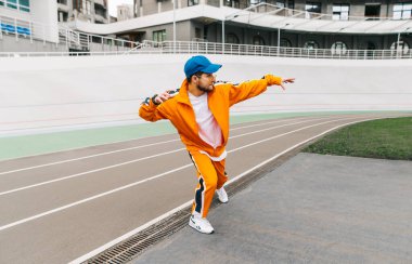 Stadyum atletizm pistinde dans eden pembe eşofmanlı parlak bir dansçının portresi. Çocuk parkında modern dans eden şık bir adam. Sokak dansı.