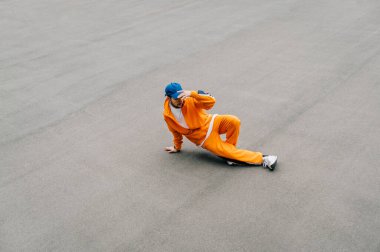 Şık bir sokak dansçısı hip hop dansı eğitiyor ve kaldırımlı oyun alanı, en üst düzey manzara, izole edilmiş. Turuncu eşofmanlı şık bir adam asfalt fondüsünde break dans yapıyor. Arkaplan